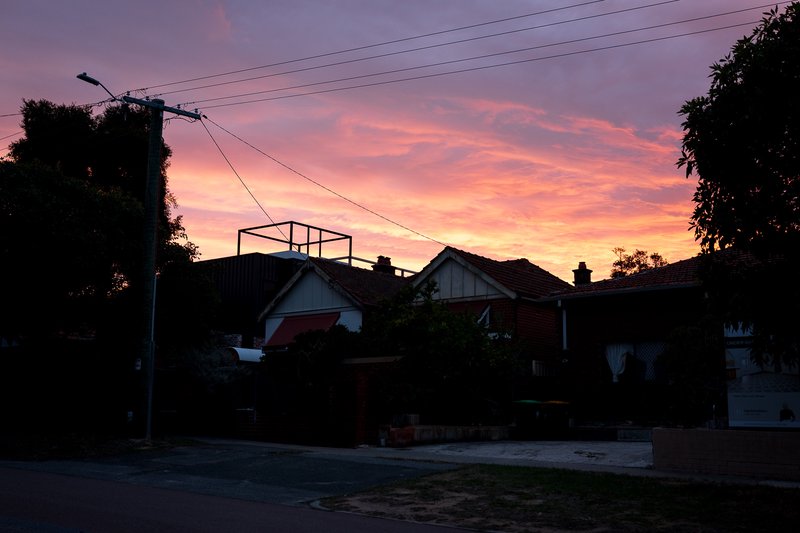A suburban street is illuminated by a vibrant sunset, casting a warm glow over the scene.