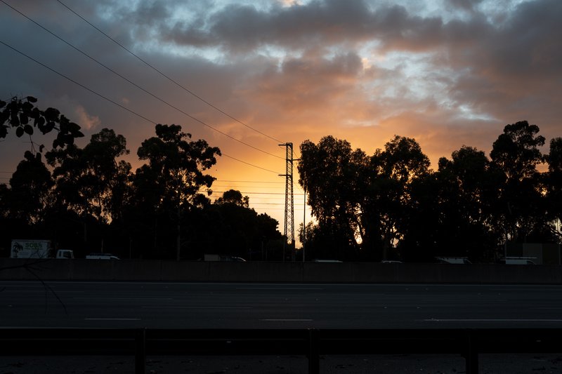 A sunset over a highway, with trees and power lines in the background.