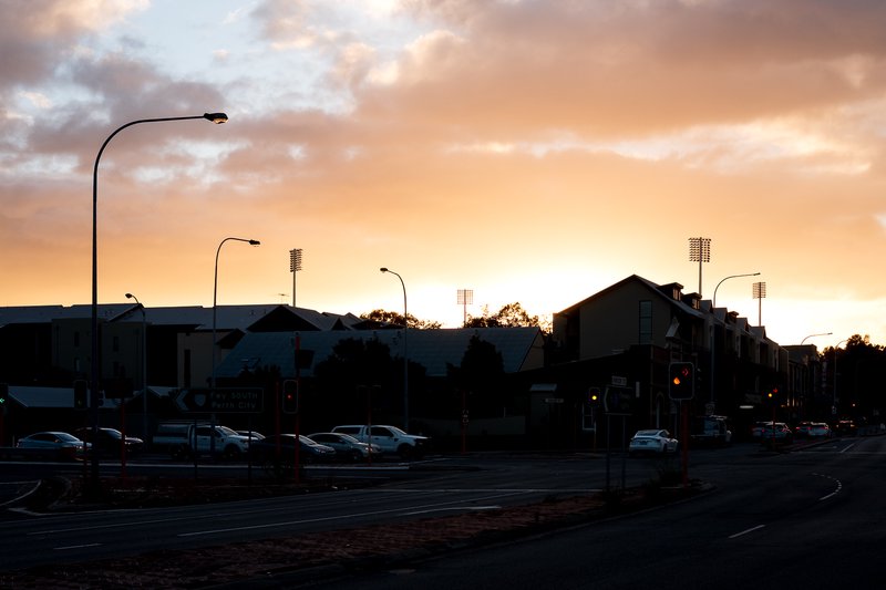 A street scene at sunset, with a building and a few cars in the background.