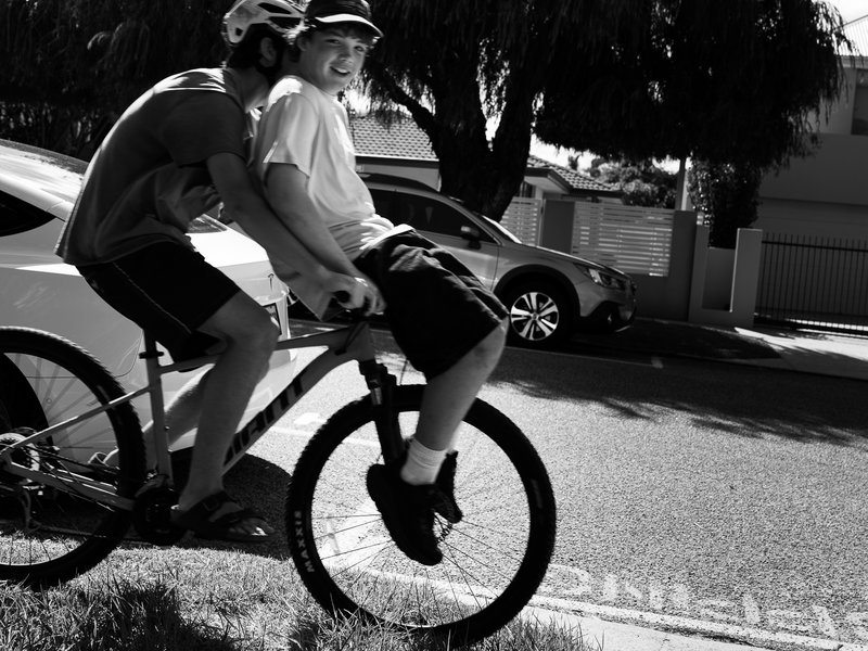 Two men riding a tandem bicycle on the side of a road, wearing helmets.