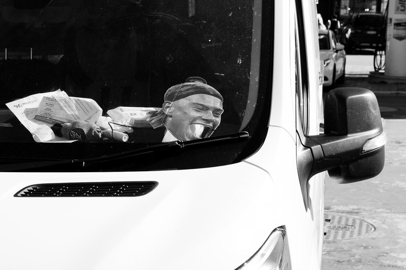 A black and white image of a truck's side mirror and a mask in the window.
