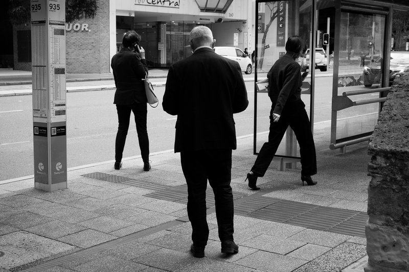 A man in a suit walks past a bus stop on a city street.