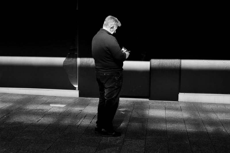 A man stands on a tiled surface, looking at his phone.