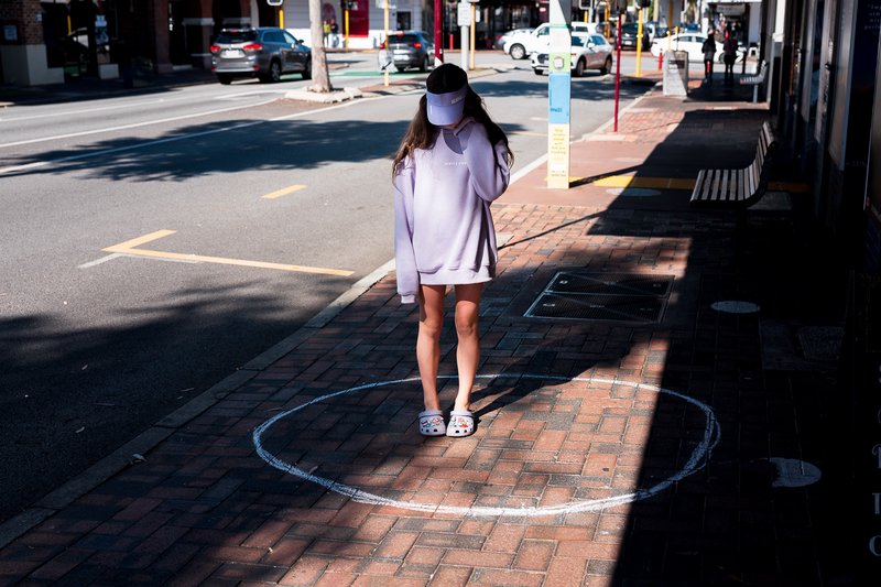 A young girl stands in a circle drawn in chalk on the sidewalk, covering her face.