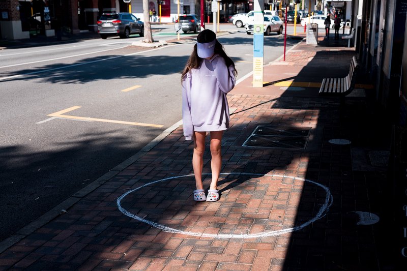 A young girl stands in a circle drawn in chalk on the sidewalk, covering her face.
