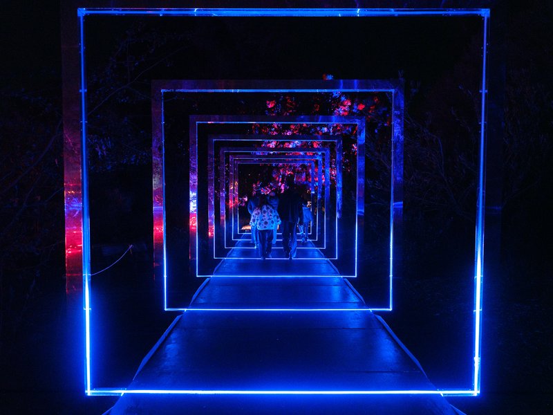 A tunnel of blue light with people walking through it at night.