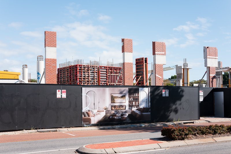Construction site with red brick pillars and modern interior advertisement on fence.