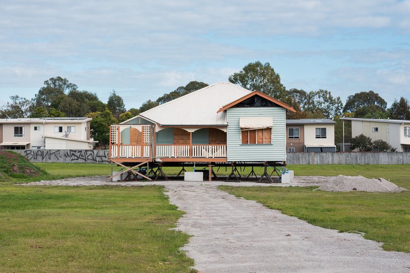 Light blue house elevated on stilts, surrounded by grass and other homes.