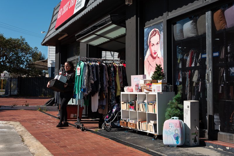 Woman shops at Red Cross store, browsing clothes and books under bright sun.