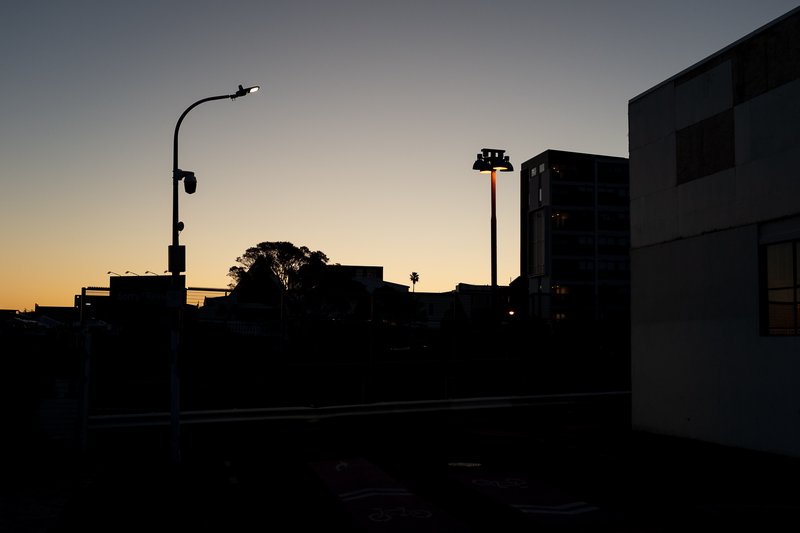 Silhouetted cityscape at dusk with streetlights and buildings against a fading sky.