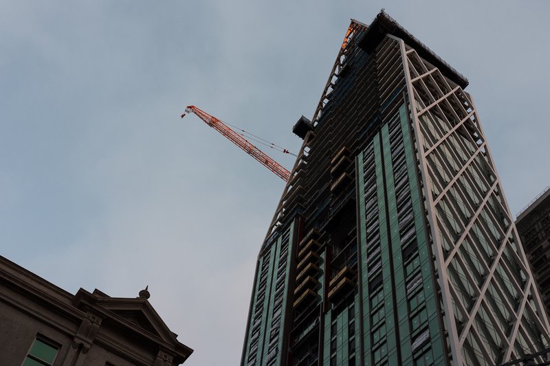 Orange crane lifts materials against a modern skyscraper under construction.