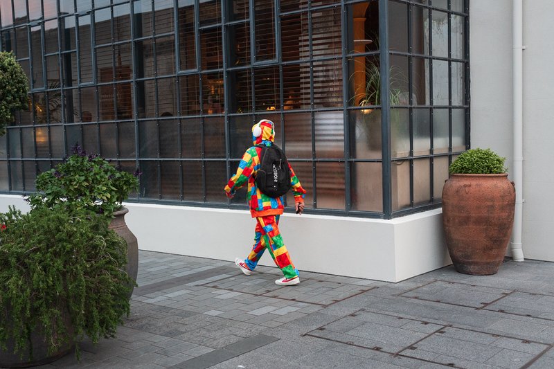 Person in colorful Lego-patterned outfit walks past modern building windows.