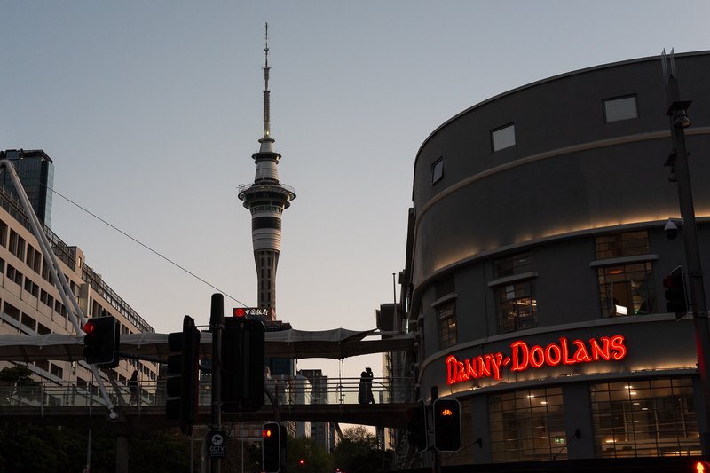Sky Tower rises above cityscape with illuminated Danny Doolans sign.