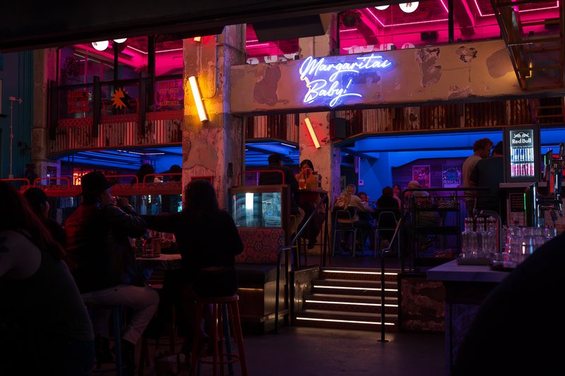 Vibrant neon-lit bar with patrons enjoying drinks under colorful lights.