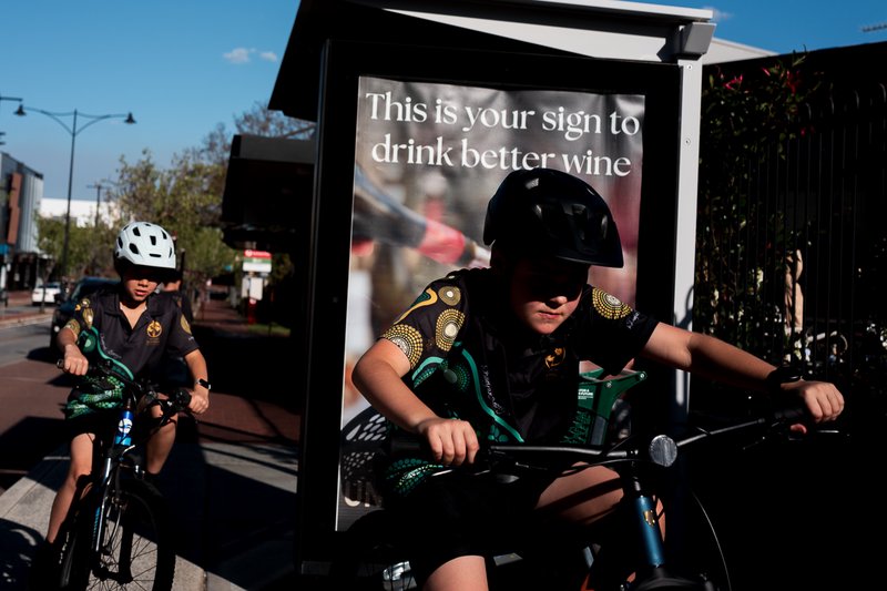 Two cyclists in matching uniforms pause near a wine advertisement sign.