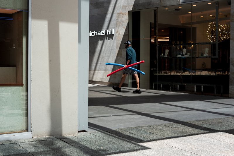 Man walks past Michael Hill store, carrying red and blue pool noodles.