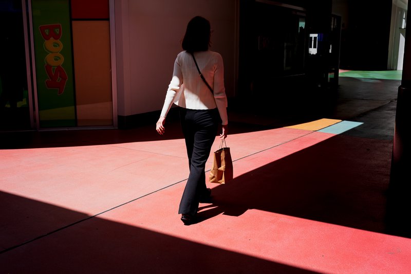 Woman walks through sunlit corridor, carrying bag and shoulder strap.